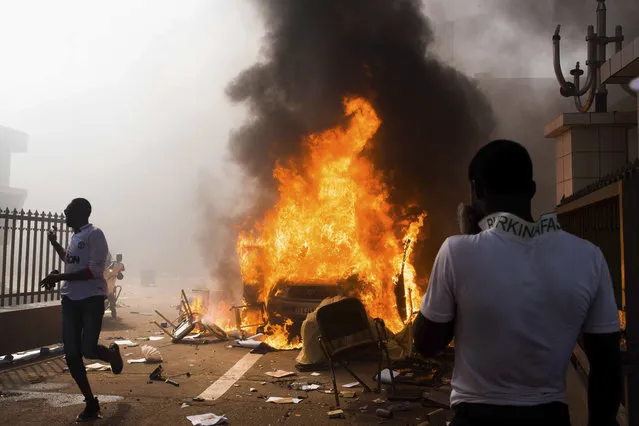 In this photo taken Thursday, October 30, 2014, a car burns after being set alight by protesters outside the parliament building in Burkina Faso as people protest against their longtime President Blaise Compaore who seeks another term, in Ouagadougou, Burkina Faso. (Photo by Theo Renaut/AP Photo)