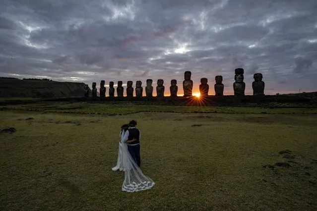 Chilean newlyweds Daniela Figueroa and Ricardo Torres, from Puerto Montt, Chile, look at moais statues at sunrise as they get cell phone photos taken by their tour guide on Ahu Tongariki, Rapa Nui, or Easter Island, Chile, Tuesday, November 22, 2022. (Photo by Esteban Felix/AP Photo)