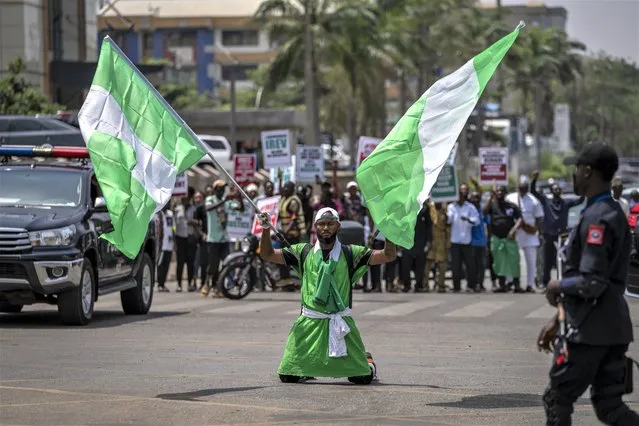A demonstrator holds two Nigerian flags as he and others accusing the election commission of irregularities and disenfranchising voters make a protest in downtown Abuja, Nigeria, Tuesday, February 28, 2023. Tensions rose in Nigeria Tuesday as the main opposition parties demanded a revote for the country's presidential election, where the latest results show an early lead for the ruling party. (Photo by Ben Curtis/AP Photo)