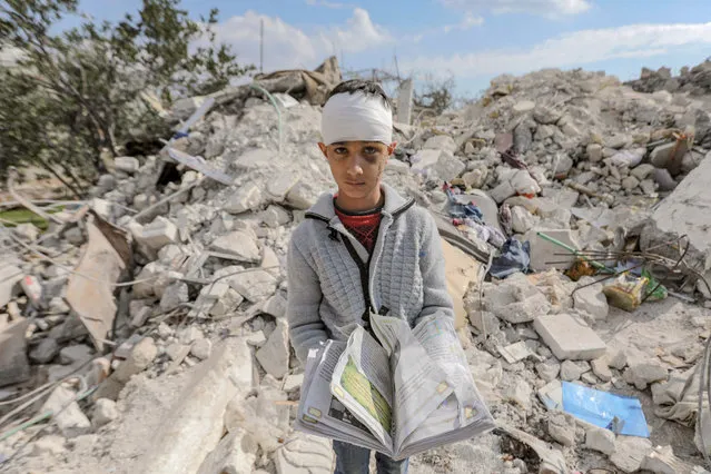 A Syrian boy, who lost his family and was also wounded as a result of the deadly earthquake hit Turkey and Syria, carries a book as he stands amid the rubble of his family home in the town of Jindayris, in the rebel-held part of Syria's Aleppo province on February 11, 2023. (Photo by Bakr Alkasem/AFP Photo)