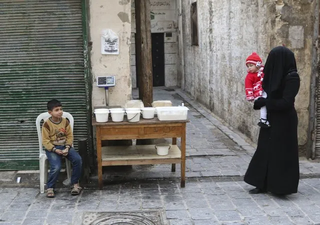 A woman carries a child as she walks past a boy selling yogurt along a street in Aleppo's Bab al-Hadeed district December 10, 2014. (Photo by Mahmoud Hebbo/Reuters)