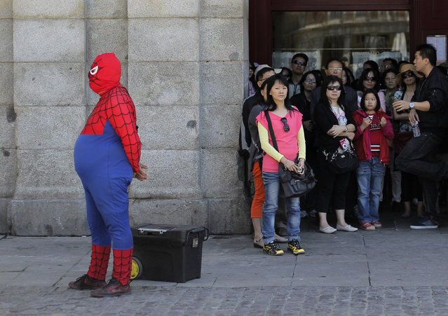 A man wearing a spiderman outfit performs for money as tourists look at the main square in Madrid, Spain, Thursday, May 23, 2013. Financial markets around the world were roiled Thursday after Japanese stocks suffered their biggest reverse since the tsunami that hit the country over two years ago. Spain has had to pay higher interest rates on selling euros 4 billion euros ($5.2 billion) in a bond auction that coincided with a sharp drop in global financial markets on worries over China's economy. Spain's Ibex 35 stock index was down 2 percent. (Photo by Andres Kudacki/AP Photo)