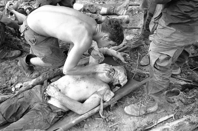 A medic offers a seriously wounded friend a cigarette as he waits for medical evacuation following a North Vietnamese ambush while sweeping through heavy jungle west of Dau Tieng, 40 miles northwest of Saigon in Vietnam, May 15, 1969. The armored unit was hit late in the day after sweeping an area hit by B-52 strikes earlier. Two armored companies were hit by an estimated battalion of NVA hidden in well-fortified bunkers. (Photo by Oliver Noonan/AP Photo)