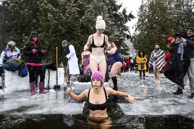 People enter the water through a hole cut in the ice at Gatineau Park's Meech Lake in Chelsea, Que., during a polar bear dip on New Year's Day, Wednesday, January 1, 2025. (Photo by Justin Tang /The Canadian Press via AP Photo)