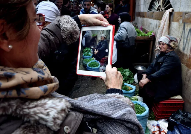 In this Saturday, January 17, 2015 photo, a tourist from Argentina takes a photograph with her tablet computer of a woman selling foraged greens, during a day trip in the northern city of Tripoli, Lebanon. “Foreigners!” residents called out to each other as the group of around 30 Lebanese and foreign tourists made their way through the Old City's labyrinth of cobblestone alleys, snapping pictures of centuries-old archways and graceful minarets. (Photo by Bilal Hussein/AP Photo)