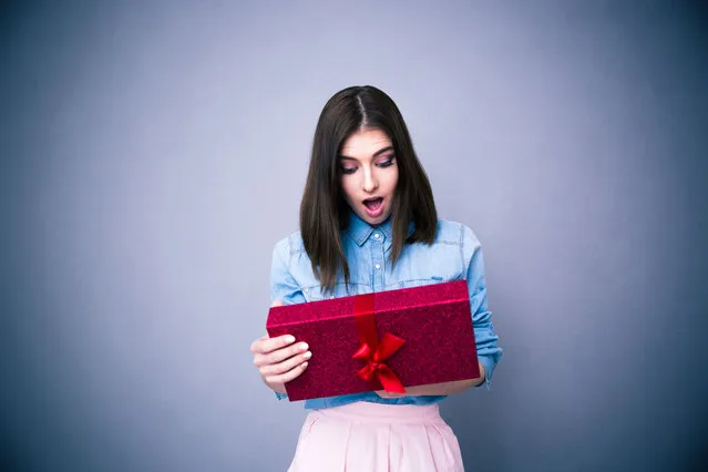 Shocked woman looking at gift over gray background. (Photo by Dean Drobot/Getty Images/iStockphoto)