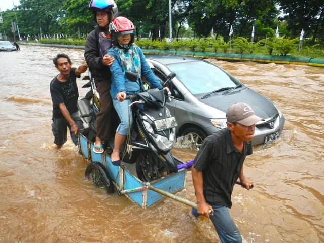 A couple sitting on their motorcycle cross a flooded road on a cart in Jakarta on February 10, 2015. Heavy monsoon rains have flooded many sections of the Indonesian capital causing heavy traffic and leaving some commuters stranded. (Photo by Bay Ismoyo/AFP Photo)