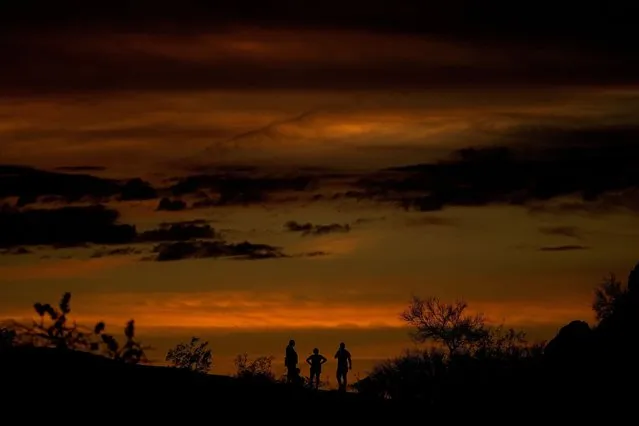 People watch the stand atop a rock formation to watch sunset, July 30, 2023, in Phoenix. At about summer's halfway point, the record-breaking heat and weather extremes are both unprecedented and unsurprising, hellish yet boring in some ways, scientists say. (Photo by Matt York/AP Photo)