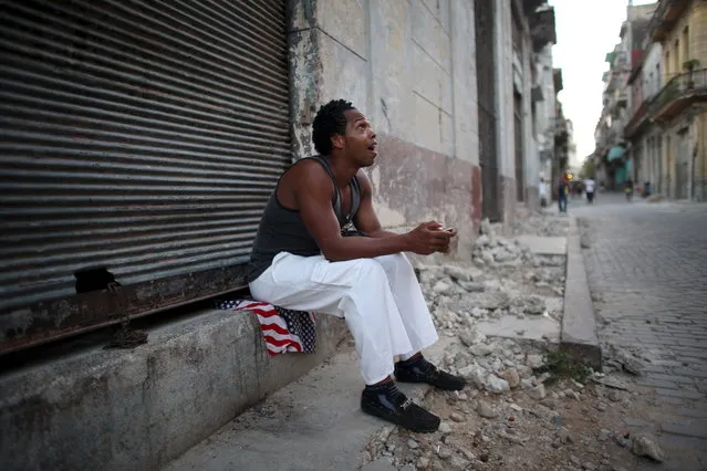 Dancing teacher Yeni Acosta, 19, sits on the sidewalk as he chats on his mobile phone in downtown Havana, August 6, 2015. (Photo by Alexandre Meneghini/Reuters)