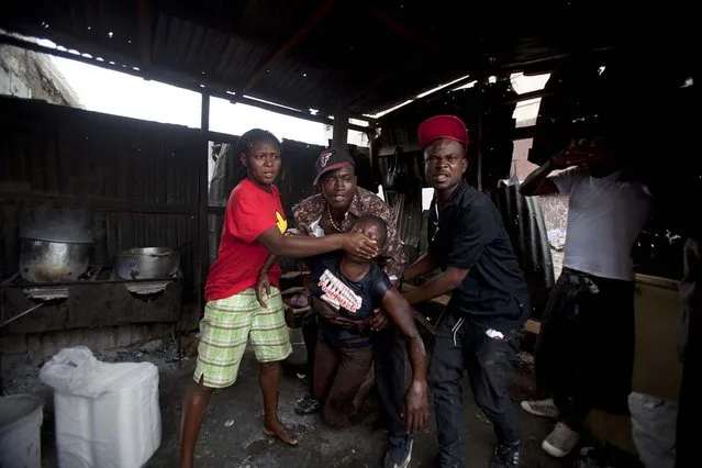 People help a street vendor who took refuge inside a restaurant to escape tear gas being fired by police breaking up a protest in Port-au-Prince, Haiti, on September 30, 2013. Police broke up the end of an anti-government demonstration by people marking the anniversary of the 1991 ouster of former President Jean-Bertrand Aristide. (Photo by Dieu Nalio Chery/Associated Press)