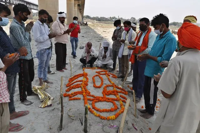 Family members and relatives of a person who died of reasons other than COVID-19 pray next to his shallow sand grave on the banks of river Ganges in Prayagraj, India, Sunday, May 16, 2021. (Photo by Rajesh Kumar Singh/AP Photo)