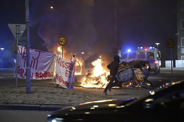 A person runs past a burning car and a banner reading,  “No to Quran burning. Don't abuse freedom of expression” placed on the roundabout, at Ramel väg, in Malmo, Sweden, early Monday September 4, 2023.  Clashes in an immigrant neighborhood in Sweden’s third largest city after an anti-Muslim protester set fire to the Quran with police being pelted with rocks and dozens of cars set on fire. Police said Monday, adding the tensions now have died down. (Photo by Johan Nilsson /TT News Agency via AP Photo)