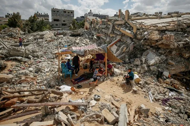 Palestinians sit in a makeshift tent amid the rubble of their houses which were destroyed by Israeli air strikes during the Israel-Hamas fighting in Gaza on May 23, 2021. (Photo by Mohammed Salem/Reuters)
