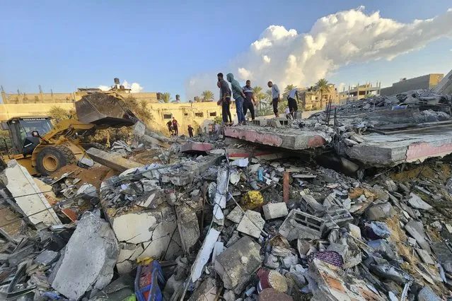 Palestinians stand by the rubble of a building destroyed in Israeli airstrikes in Deir el-Balah Gaza Strip, Sunday, October 15, 2023. (Photo by Hasan Islayeh/AP Photo)