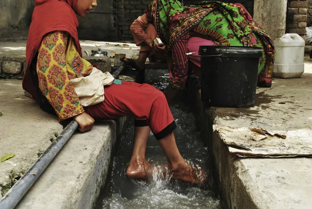 In this Monday, July 9, 2018, photo, Ansa Khan cools her feet with running water just adjacent to her home while her mother and sister are busy in their household activities and washing clothes and utensils in Mardan, Pakistan. (Photo by Saba Rehman/AP Photo)