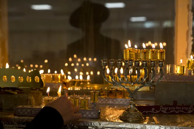 An ultra-Orthodox Jewish man lights candles during the Jewish holiday of Hanukkah in Bnei Brak, near Tel Aviv, Israel Wednesday, December 28, 2016. Hanukkah, also known as the Festival of Lights, is an eight-day commemoration of the Jewish uprising in the second century B.C. against the Greek-Syrian kingdom, which had tried to put statues of Greek gods in the Jewish Temple in Jerusalem. (Photo by Ariel Schalit/AP Photo)
