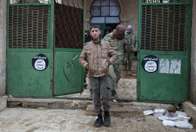 Rebel fighters walk out of a mosque in al-Rai town, northern Aleppo countryside, Syria December 30, 2016. On the gate are seen Islamic State logo stickers. (Photo by Khalil Ashawi/Reuters)