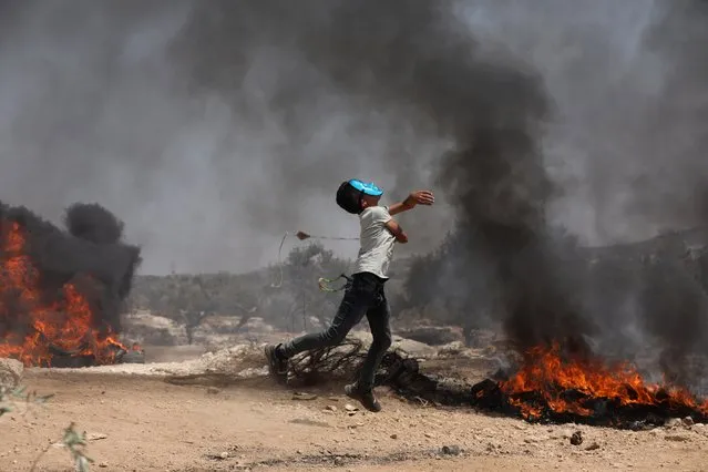 Palestinian protester wearing a mask uses slingshot to hurl stones during clashes after a demonstration against the expansion of the new Jewish outpost of Eviatar on the lands of Beita village near the West Bank City of Nablus, 30 July 2021. According to Palestinian medics, 46 people were wounded during the clashes. (Photo by Alaa Badarneh/EPA/EFE)
