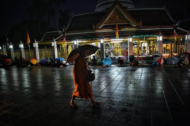 A Buddhist monk walks past people queueing overnight for free Covid-19 swab testing at Wat Phra Sri Mahathat Woramahawihan in Bangkok, in the early hours of the morning on July 9, 2021. (Photo by Lillian Suwanrumpha/AFP Photo)