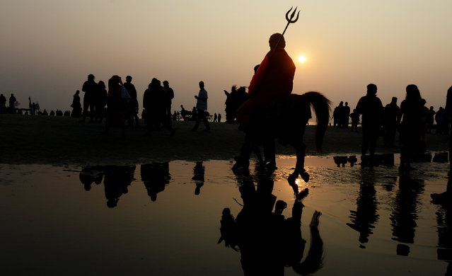 An Indian sadhu – Hindu holy man – rides on a horse to take a holy bath and perform rituals at the Gangasagar Island, around 150 kms south of Kolkata on January 12, 2017. More than 700,000 Hindu pilgrims and sadhus – holy men – are expected to gather at the confluence of the River Ganges and the Bay of Bengal during the Gangasagar Mela to take a 'holy dip' in the ocean on the occasion of Makar Sankranti, a holy day of the Hindu calendar considered to be of great religious significance in Hindu mythology. (Photo by Dibyangshu Sarkar/AFP Photo)