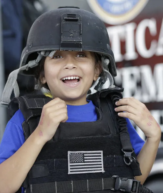 Valerie Gonzalez, 5, a student at The Growing Place preschool in Coral Gables, Fla., smiles as she tries on a tactical vest and helmet during an open house event at Coast Guard Air Station Miami, Friday, April 17, 2015, in Opa-Locka. About 1,500 students from Miami-Dade and Broward County schools attended the event where they could climb aboard various aircraft and vessels used by the Coast Guard and other law enforcement agencies. (Photo by Wilfredo Lee/AP Photo)