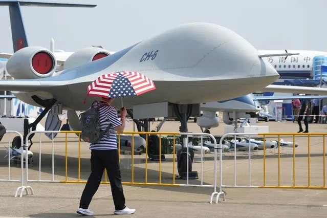 A man carrying an umbrella with the United States flag colors as he walks past the CH-6 drone during the 13th China International Aviation and Aerospace Exhibition, also known as Airshow China 2021 onTuesday, September 28, 2021, in Zhuhai in southern China's Guangdong province. A state-owned Chinese aerospace company unveiled the military drone it says can stay aloft for up to 20 hours at altitudes as high as 15,000 meters (50,000 feet) at the opening Monday of the country's biggest air show. (Photo by Ng Han Guan/AP Photo)
