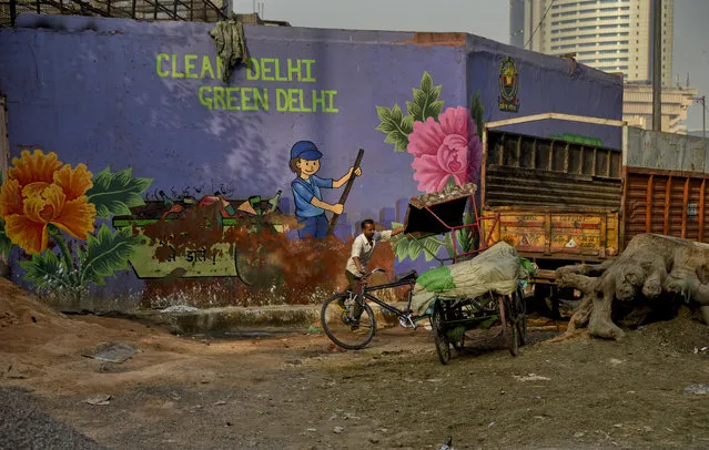 In this October 10, 2018, photo, an Indian cycle rickshaw puller maneuvers his rickshaw past an awareness mural campaigning for a clean and green Delhi in New Delhi, India, Wednesday. Huge sums have been spent on a marketing blitz, including videos of Bollywood stars sweeping the streets, for the government's ambitious Swachh Bharat, or Clean India, program launched by Modi in 2014. (Photo by R.S. Iyer/AP Photo)