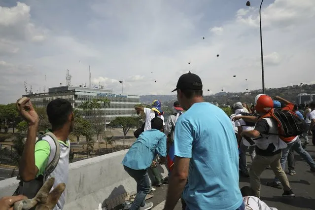 Anti-government protesters launch rocks to National Guard forces outside La Carlota airbase during clashes between the two sides in Caracas, Venezuela, Wednesday, May 1, 2019. (Photo by Rodrigo Abd/AP Photo)