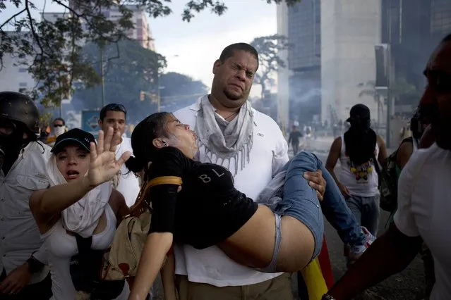 A man carries a woman affected by tear gas launched by riot police at anti-government protesters in Caracas, Venezuela, Saturday, February 22, 2014. After their opposition rally broke up in the late afternoon, in a pattern that has been seen in past demonstrations about 1,000 stragglers erected barricades of trash and other debris and threw rocks and bottles at police and National Guardsmen. (Photo by Rodrigo Abd/AP Photo)