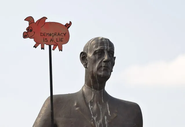 A cartoon pig shaped banner that reads: “Democracy is a Lie” is held next to the statue of French General and former President Charles de Gaulle during a protest against illegal logging in Bucharest, Romania, Saturday, May 9, 2015. (Photo by Vadim Ghirda/AP Photo)