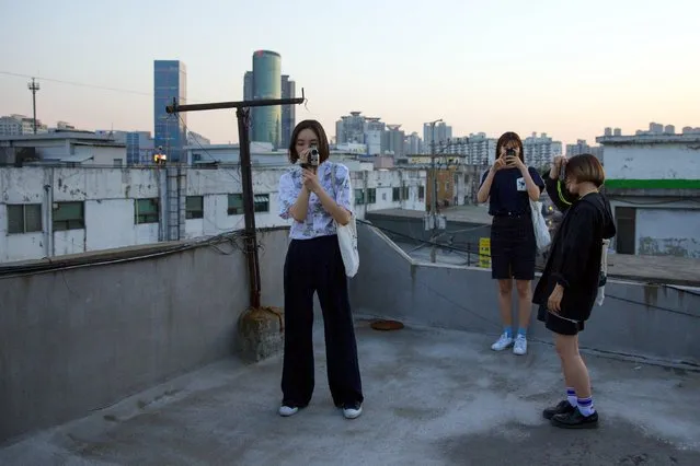 Women take pictures as they stand on the roof of a workshop in the industrial district of Mullae in Seoul, May 10, 2015. (Photo by Thomas Peter/Reuters)