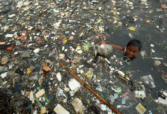 A boy collects plastic for resale at Marunda beach in Jakarta, Indonesia on February 1, 2007. The Intergovernmental Panel on Climate Change (IPCC) will release a long-awaited report assessing the human link to pollution, global warming and climate change in Paris on February 2, 2007. A draft of the report, which draws on research by 2,500 scientists from more than 130 countries, projects a big rise in temperatures this century and warns of more heatwaves, floods, droughts and rising sea levels linked to greenhouses gases released mainly by the use of fossil fuels. (Photo by Reuters/Beawiharta)