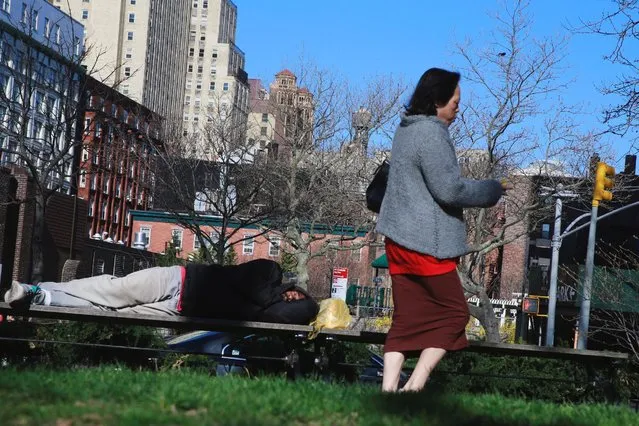 A woman looks at her phone as she walks past a man sleeping on a bench in the Brooklyn borough of New York, April 13, 2016. (Photo by Lucas Jackson/Reuters)