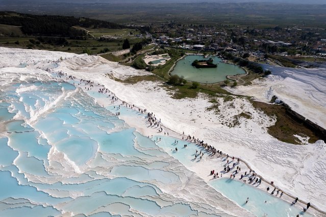 An aerial view of Pamukkale, a UNESCO World Heritage Site known for its mineral-rich thermal waters flowing down white travertine terraces on a nearby hillside, during the spring season in Denizli, Turkiye on May 06, 2024. Thermal waters have been flowing at Pamukkale for 2500 years. Despite the hot weather, the limestone and travertine layers of Pamukkale attract many tourists. (Photo by Ahmet Aslan/Anadolu via Getty Images)