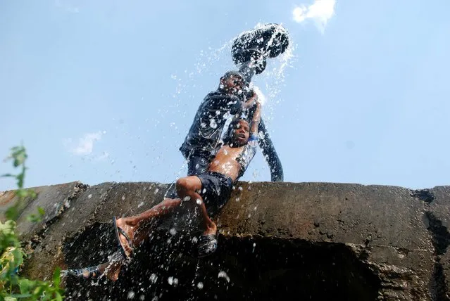 Indian children cool off as water water flows from a water supply pipeline to beat the heat on a hot afternoon on the outskirts of eastern Bhubaneswar on April 28, 2014.  Many Indian cities face severe water scarcity especially in the summer season as summer temperatures soar above the 40 degrees celsius. (Photo by Asit Kumar/AFP Photo)