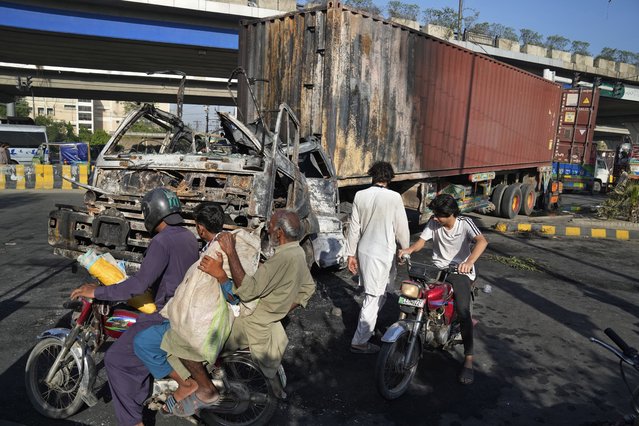 Motorcyclists ride past a truck burnt during clashes with police and the supporters of Pakistan's former Prime Minister Imran Khan, at a road, in Lahore, Pakistan, Thursday, May 11, 2023. Pakistan's government called out the military Wednesday in areas roiled by deadly violence following the arrest of former Prime Minister Imran Khan, who was dragged from a courtroom and ordered held for another eight days on new corruption charges that outraged his supporters and deepened the country's political turmoil. (Photo by K.M. Chaudary/AP Photo)