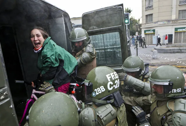 In this Wednesday, June 21, 2017 photo, a woman, while on her bicycle, is lifted and placed by police into a paddy wagon during a protest march demanding the government overhaul the education funding system that would include canceling their student loan debt, in Santiago, Chile. (Photo by Esteban Felix/AP Photo)