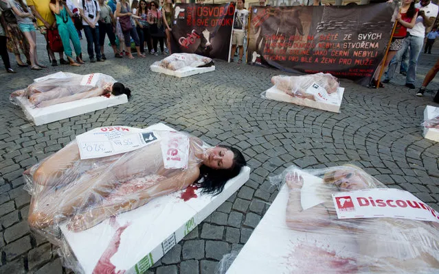 Half-naked animal rights activists packed like a portions of fresh meat for a supermarket lay on pavement in downtown Prague, Czech Republic, Friday, July 18, 2014, during a protest meeting “Animal is No Commodity” held by 269 international movement against the exploitation of animals. (Photo by Vit Simanek/AP Photo/CTK)