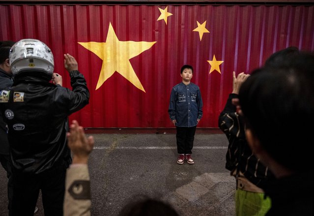 A young boy stands in front of a large Chinese national flag painted on the side of a container at an outdoor market during the Golden Week holiday on October 3, 2024 in Beijing, China. China marked its National Day and the 75th anniversary of the founding of the Peoples Republic on October 1st. (Photo by Kevin Frayer/Getty Images)