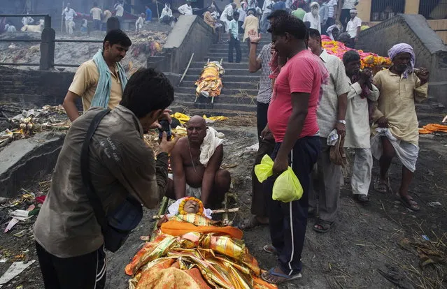 A man poses for a photograph with the body of a deceased relative prior to cremation on the banks of river Ganges in Varanasi, in the northern Indian state of Uttar Pradesh, June 19, 2014. (Photo by Danish Siddiqui/Reuters)