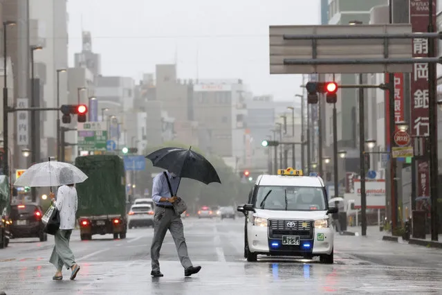 People walk in the rain in front of a station, Saturday, August 13, 2022, in Shizuoka, west of Tokyo. Tropical Storm Meari is unleashing heavy rains on southwestern Japan as it heads northward toward the Tokyo capital, according to Japanese weather officials. (Photo by Kyodo News via AP Photo)