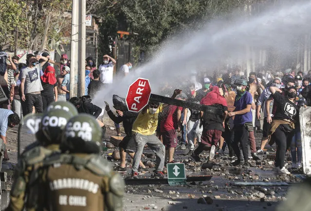 Demonstrators, some wearing protective face masks amid the new coronavirus pandemic, clash with the police during a protest demanding food aid from the government, at a poor neighborhood in Santiago, Chile, Monday, May 18, 2020. (Photo by Esteban Felix/AP Photo)