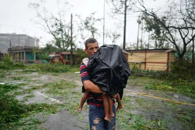 A man carries his children next to debris caused by the Hurricane Ian after it passed in Pinar del Rio, Cuba on September 27, 2022. (Photo by Alexandre Meneghini/Reuters)