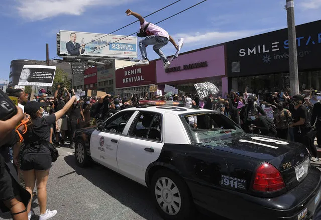 A demonstrator jumps on a police car during a protest over the death of George Floyd, Saturday, May 30, 2020, in Los Angeles. Protests were held throughout the country over the death of George Floyd, a black man who died after being restrained by Minneapolis police officers on May 25. (Photo by Mark J. Terrill/AP Photo)