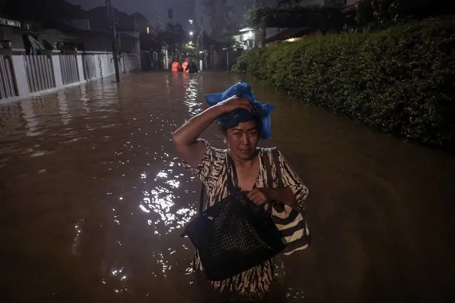 A woman makes her way through a street flooded due to heavy rain in a residential area in Jakarta on October 6, 2022. (Photo by Andre May/AFP Photo)