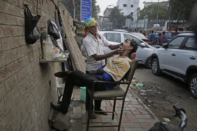 In this November 15, 2017, photo, Dinesh, 55, who has been working for the last 20 years as a roadside barber attends to a customer in New Delhi, India. Dinesh, who uses only one name, sets up a mirror and chair on the sidewalk and typically earns about 100 rupees ($1.50) a day cutting men’s hair and shaving them. He said he often thinks about returning to his family farm in the northeastern state of Bihar.“I’m a poor man who is doing my work”, he said. “I have to feed my kids”. He said if he had any spare money he would think about buying a pollution mask. What he does earn, he said, he spends on basics like salt and chapatti, a type of Indian bread. “I’m old now. I will go to my home and do some farming, plow my field”, he said. “What else can I do?”. (Photo by Altaf Qadri/AP Photo)