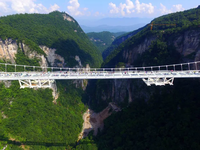 Visitors walk across a glass-floor suspension bridge in Zhangjiajie in southern China's Hunan Province Saturday, August 20, 2016. (Photo by Chinatopix via AP Photo)
