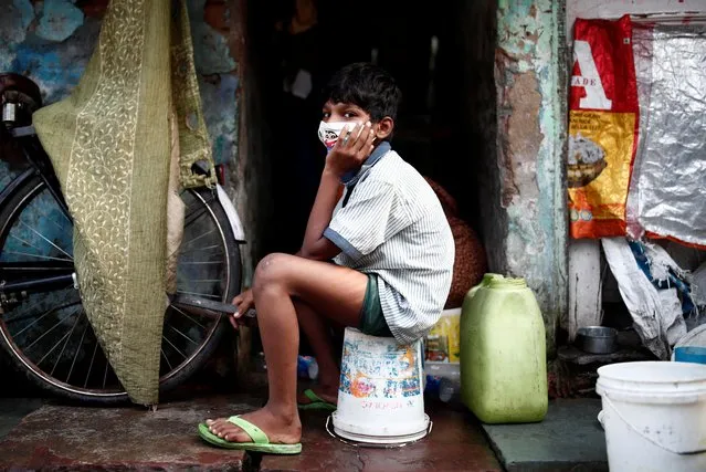 A boy wearing a protective face mask sits on a bucket outside a house in a slum area, during an extended nationwide lockdown to slow the spreading of the coronavirus disease (COVID-19), in New Delhi, India, June 24, 2020. (Photo by Adnan Abidi/Reuters)