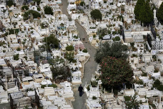 In this Oct. 14, 2014, photo, a Lebanese man, center, walks between graves at the overcrowded Bashoura cemetery for Muslim Sunnis in Beirut, Lebanon. The congested city of more than one million is cramped with cemeteries wedged into residential areas, increasingly forcing families to bury several members of the same family in one grave. Available land plots are extremely scarce and what is left is being used by developers to build luxury officers towers and apartments. (AP Photo/Hussein Malla)