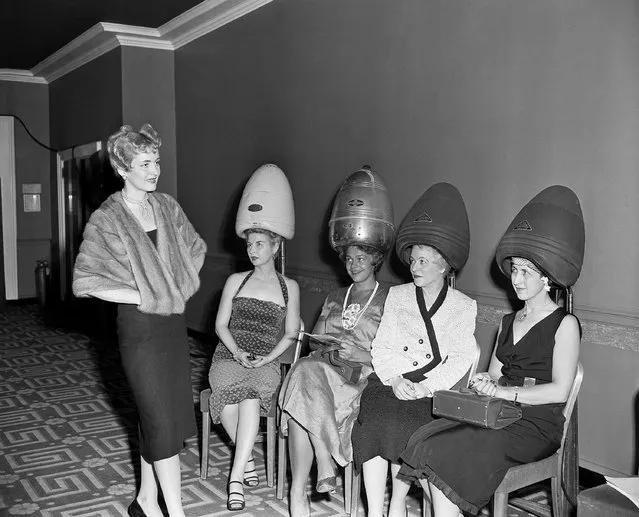 Four hairdressers attending the National Beauty Trades Show in New York 'cool off' under hair driers in an air-conditioned room at the Hotel Statler on September 1, 1953 while Erma Van Wort, in a sable cape, shows them a new mobile coiffure. The hair driers' temperature is a mere 90 degrees, while the official thermometer outdoors measured 97. The new hairdo, achieved with free-flowing waves, is designed to direct eyes to the head - whatever the length of the controversial hemline. The hairdressers are members of the National Hairdressers and Cosmetologists Association. (Photo by Carl Nesensohn/AP Photo)